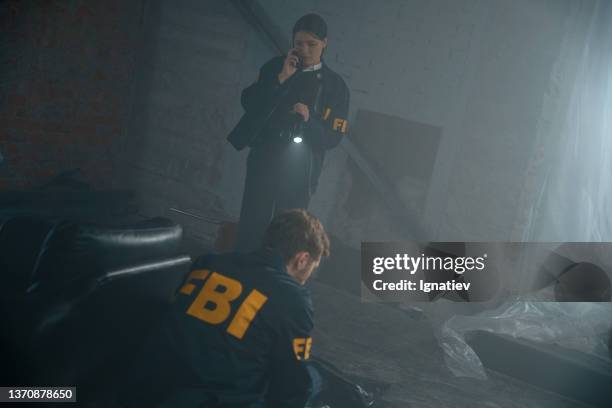 fbi agents at work. calling special services on the phone looking at the dead body on the crime scene in abandoned warehouse - female fbi stock pictures, royalty-free photos & images