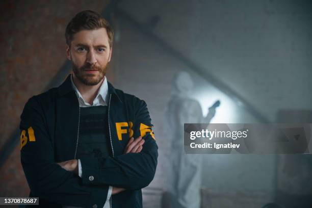 gutaussehender fbi-agent, der mit verschränkten armen am tatort steht, er schaut in die kamera, wir sehen ihn von der taille aufwärts - kriminologie stock-fotos und bilder