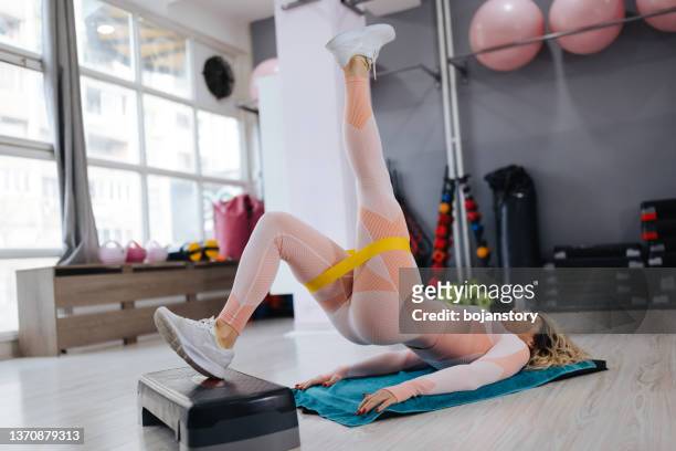 young sportswoman doing glute bridge exercise with fitness band in health club - buttock stockfoto's en -beelden