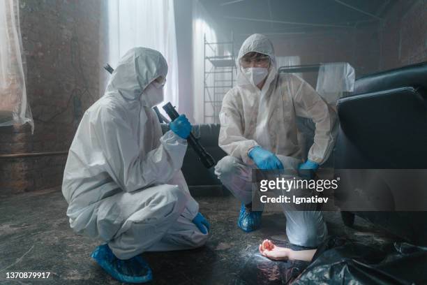 criminologists working at the crime scene in protective suits in abandoned warehouse squatting near the dead body, we see them in a daylight - criminology stock pictures, royalty-free photos & images