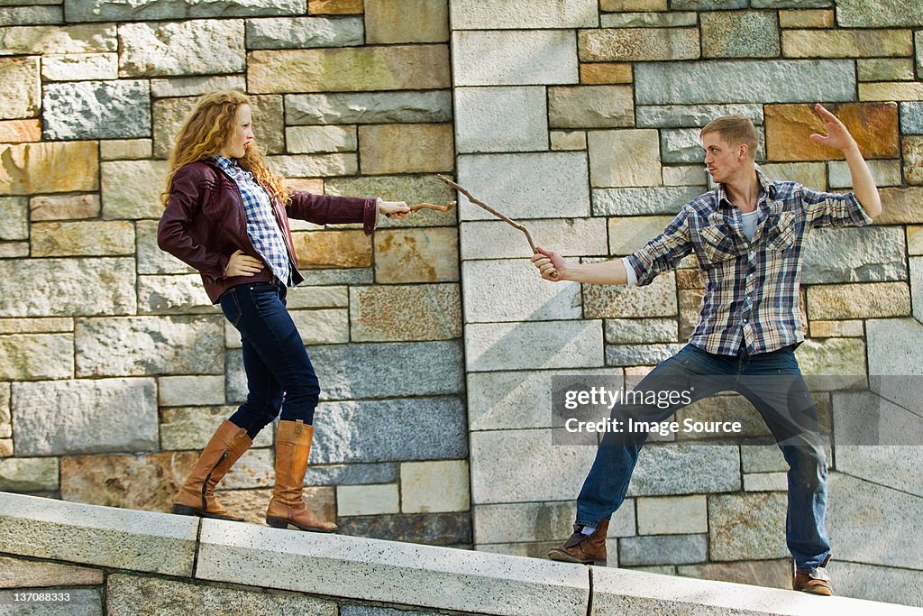 Paar Spielen, Kämpfen mit Säbeln vor Steinmauer