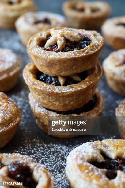 close-up image of pile homemade, mince pies, surrounded by festive christmas dessert of crispy pastry filled with sweet mincemeat, star shaped pastry top sprinkled with icing sugar, grey background, focus on foreground - christmas mince pies stock pictures, royalty-free photos & images