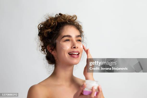 eine schöne lächelnde frau trägt anti-aging und feuchtigkeitsspendende gesichtscreme auf - anti age stock-fotos und bilder