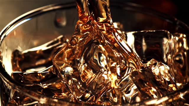 A jet of whiskey with splashes flows into a glass of ice.Filmed is slow motion 1000 fps.
