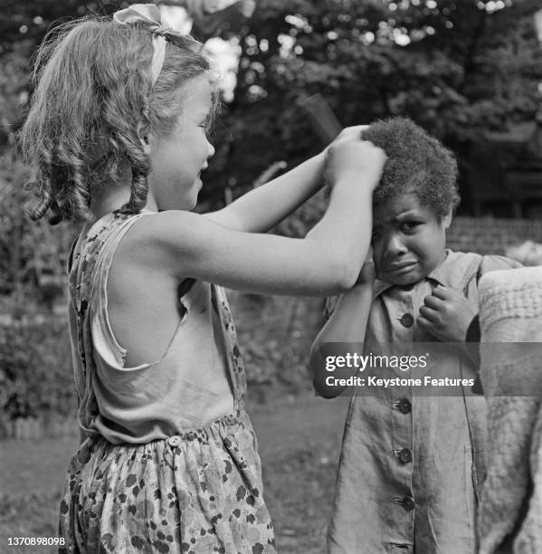 Ann Bellow doesn't seem too happy at Susan Bradley combing her curly hair, Kilburn, London, UK, 1948. They both are foster children under the care of...