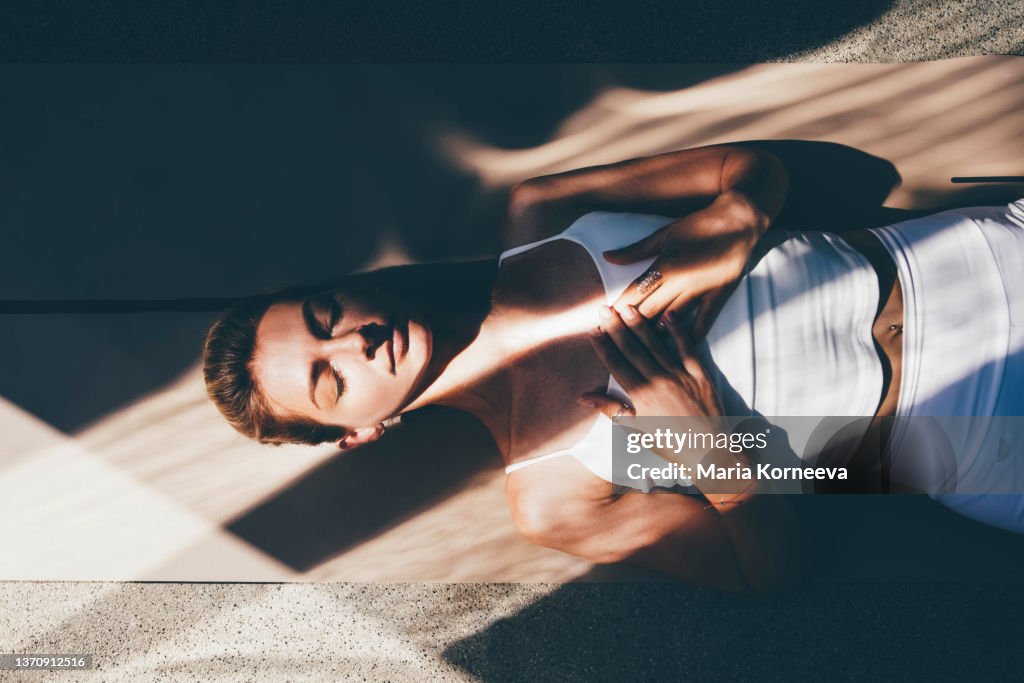 Graceful slim woman trainer in white sportswear practices yoga exercises on floor mat.