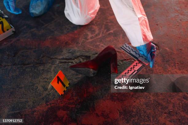 forensic scientist in protective suit measuring a physical evidence at the crime scene in a red light - crime scene stockfoto's en -beelden