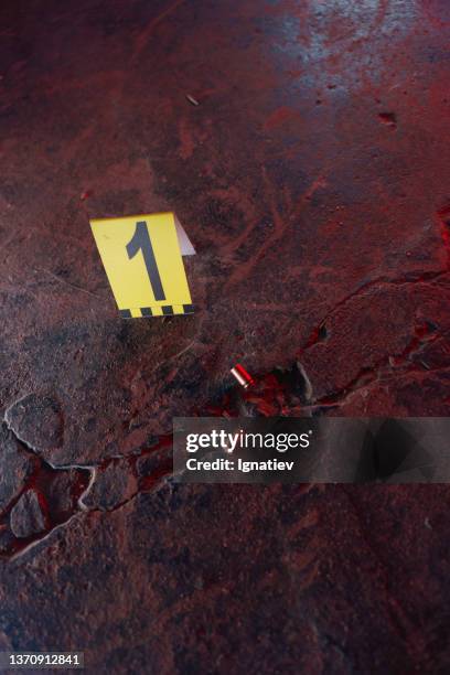 deux douilles de balles illuminées sur un sol en pierre noire en gros plan dans la lumière rouge et un numéro médico-légal à côté - murder photos photos et images de collection