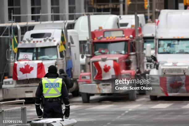 Police officer stands guard near trucks participating in a blockade of downtown streets near the parliament building as a demonstration led by truck...