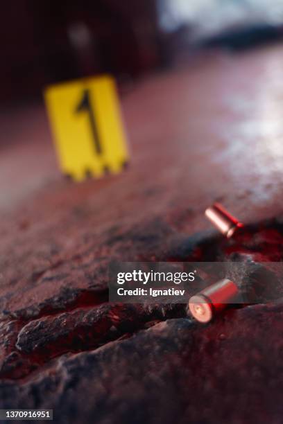 two illuminated bullet casings on a black stoned floor in close up in red light - criminology stock pictures, royalty-free photos & images