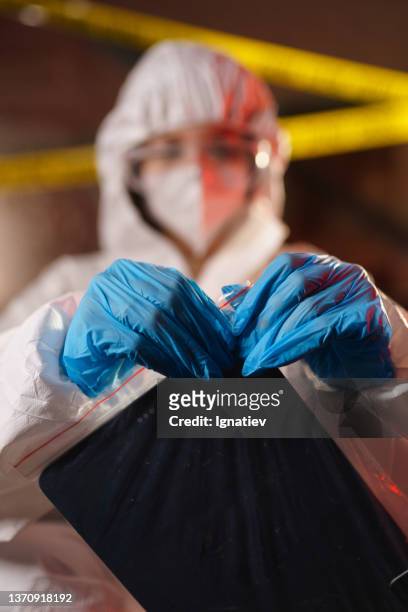 blurred close-up  of criminologist in a protective suit closing a plastic bag with a digital tablet in it as physical evidence - coroner stock pictures, royalty-free photos & images