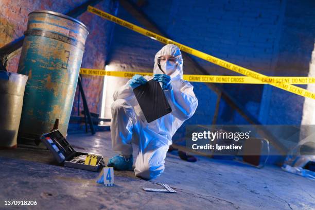 criminologist in a protective suit closing a plastic bag with a digital tablet in it as physical evidence at the crime scene - criminology stock pictures, royalty-free photos & images