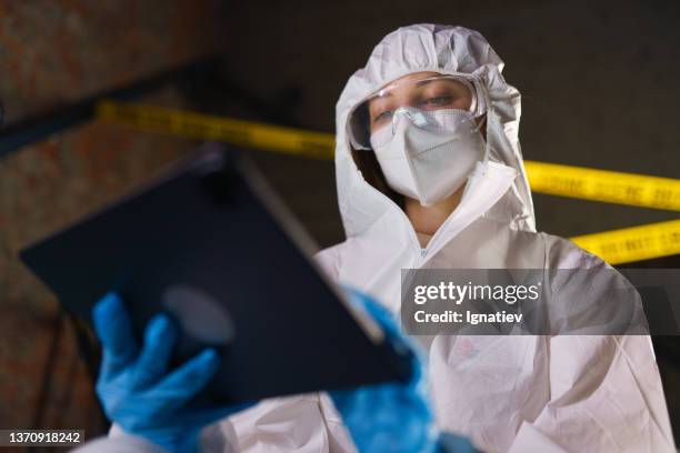 criminologist in a protective suit works on her digital tablet at the crime scene - criminology stock pictures, royalty-free photos & images