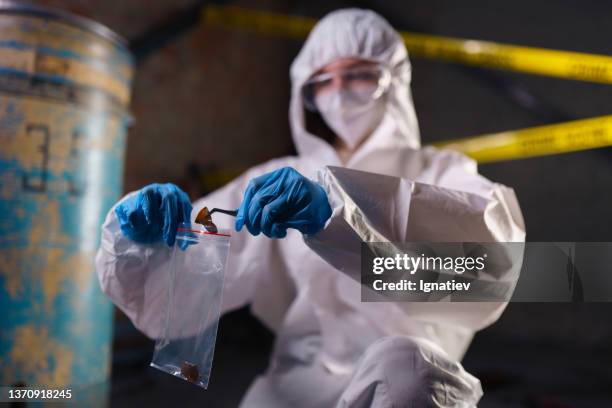 criminologist in a protective suit at the crime scene putting broken beer bottle pieces  from the floor in a plastic bag as physical evidence with forceps - finland police stock pictures, royalty-free photos & images