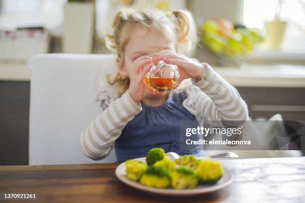 baby girl blonde in home interior , drinking apple juice and eat broccoli - apple juice stock pictures, royalty-free photos & images