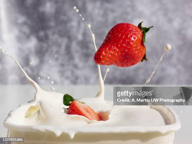 stock image of strawberries falling on yogurt cream and producing various splashes. - strawberry falling stock-fotos und bilder