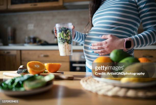young pregnant woman making a healthy smoothie. - prenatal care stock pictures, royalty-free photos & images