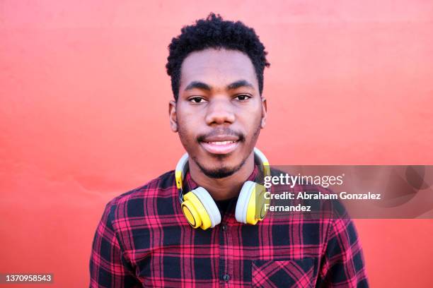 portrait of a young african-american man looking at camera with wireless headphones on his neck - headphone man on neck stock-fotos und bilder