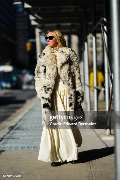 Lisa Aiken wears black sunglasses from Ray Ban, a pale yellow ribbed turtleneck t-shirt, a matching pale yellow long flowing skirt, a beige and black...