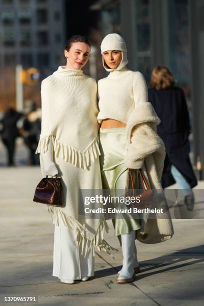 Mary Leest wears gold earrings, a white ribbed wool high neck fringed cloak, a matching white fringed wool skirt, white denim jeans wide legs pants,...