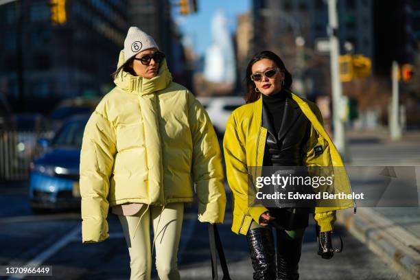 Guest wears a beige with a brown embroidered 6 pattern ribbed beanie, black sunglasses, a yellow high neck oversized puffer jacket, pale yellow slit...