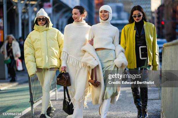 Guest wears a beige with a brown embroidered 6 pattern ribbed beanie, black sunglasses, a yellow high neck oversized puffer jacket, pale yellow slit...
