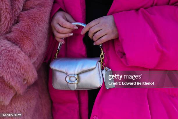 Guest wears a black knees dress, black tights, an oversized neon pink oversized long puffer jacket, a silver shiny leather handbag from Coach,...