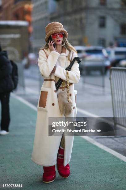 Guest wears a brown fluffy large bob, red sunglasses, gold large chain necklaces, a red asymmetric shoulder t-shirt, a white latte fluffy long coat,...