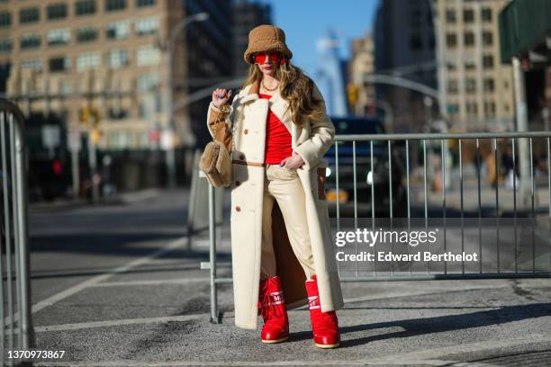 Guest wears a brown fluffy large bob, red sunglasses, gold large chain necklaces, a red asymmetric shoulder t-shirt, a white latte fluffy long coat,...
