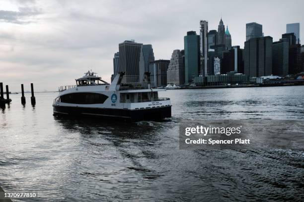 Ferry arrives into a dock as the Manhattan skyline is seen across the East River on February 16, 2022 in the Brooklyn borough of New York City. A...