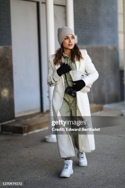 Guest wears a beige ribbed wool beanie, a brown ribbed turtleneck pullover, a khaki zipper nylon jacket, matching khaki zipper nylon pants, a white...