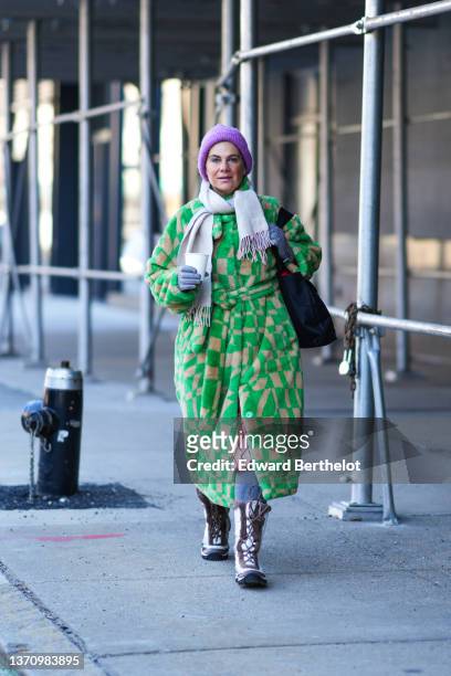 Guest wears a purple ribbed wool beanie, a beige fringed wool scarf, a green and beige print pattern belted oversized coat, a black shoulder bag,...