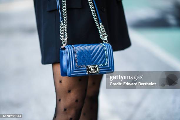 Guest wears a black oversized blazer jacket, a navy blue shiny leather Boy shoulder bag from Chanel, black shorts, black with CC monogram print...