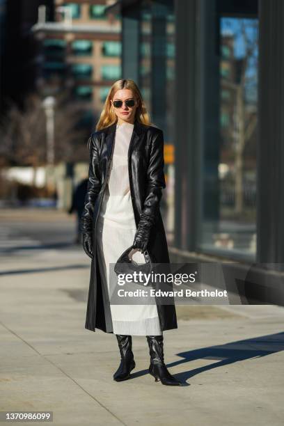 Guest wears black sunglasses, a black shiny leather long coat, black shiny leather gloves, a black shiny leather handbag, black shiny leather pointed...