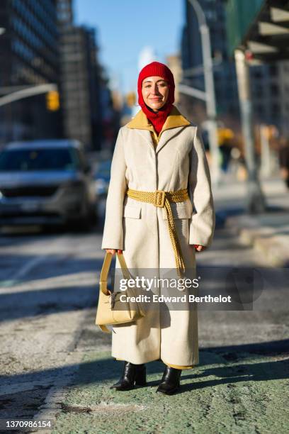 Guest wears a red ribbed wool balaclava, a brown felt jacket, a white wool long coat, brown beige large pants, a beige matte leather crocodile print...
