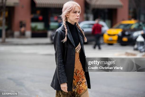 Guest is seen with pigtails wearing black leather blazer, brown dress with print, turtleneck outside Collina Strada during New York Fashion Week on...