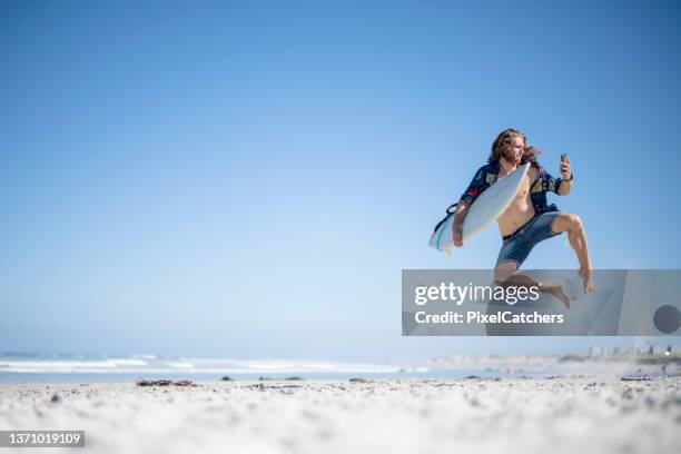 male surfer on the beach jumping in the air holding his mobile - person surfing the internet stock pictures, royalty-free photos & images