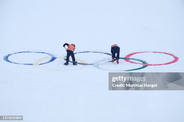 Track officials clear snow from the olympic rings during a Ski Jumping Trial Round as part of Biathlon Team Gundersen Large Hill/4x5km event on Day...