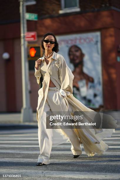 Chriselle Lim wears black sunglasses, gold earrings, a silver shiny pearls necklace, a white lace pattern V-neck cropped top, a beige long oversized...