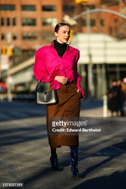 Mary Leest wears a black turtleneck pullover, a neon pink oversized shirt with pleated ruffled wrists, a black shiny leather with gold YSL buckle...