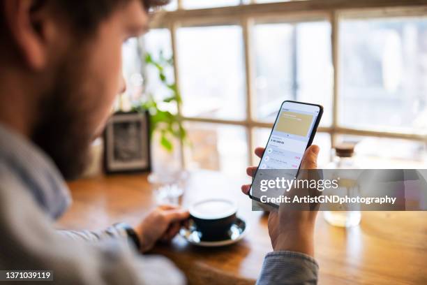 junger mann, der die finanzen auf der mobilen app verfolgt, während er kaffee trinkt. - bankkonto stock-fotos und bilder