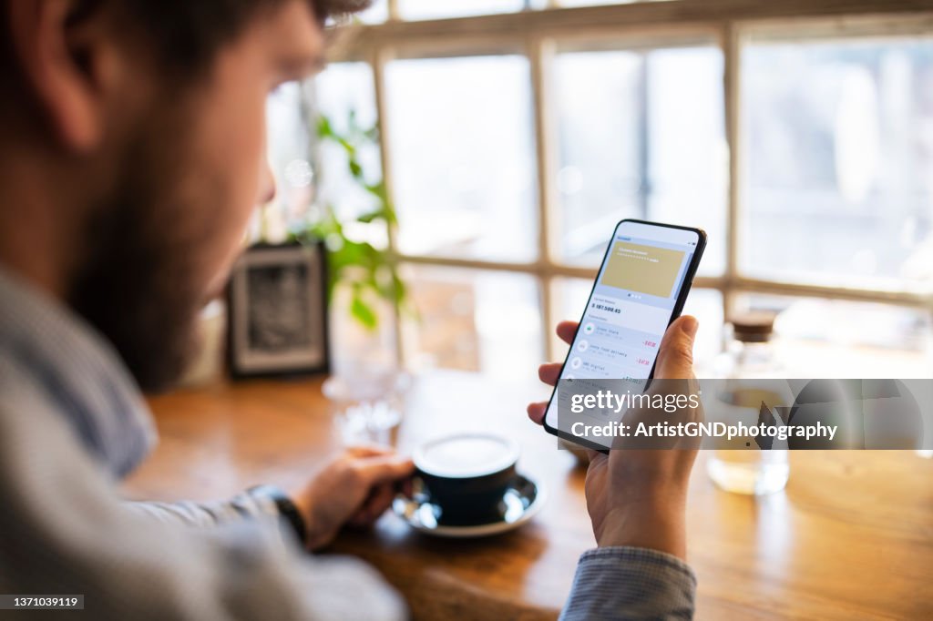コーヒーを飲みながら、モバイルアプリで金融を追跡する若い男。