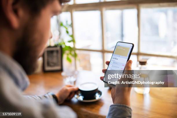 young man tracking finance on mobile app while drinking coffee. - banking industry stock pictures, royalty-free photos & images