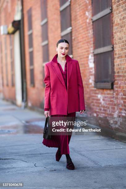 Mary Leest wears a burgundy pleated / accordion buttoned shirt, a matching burgundy pleated / accordion buttoned midi skirt, a black Re-edition 2000...