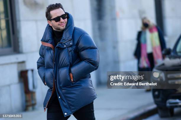 Derek Blasberg wears black sunglasses, a black turtleneck pullover, a black oversized puffer jacket, black denim jeans pants, outside Gabriela Hearst...