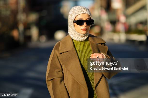 Guest wears a gray wool balaclava, black sunglasses from Lacoste, a green wool pullover, a brown oversized long coat, silver rings, outside Peter Do...