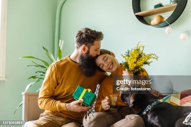 caring young man kissing his girlfriend on the head after giving her flowers - gift giving stock pictures, royalty-free photos & images