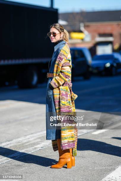 Guest wears black sunglasses, silver earrings, a black high neck pullover, a navy blue denim buttoned shirt midi dress, a camel shiny leather belt, a...