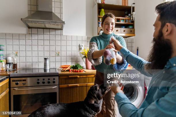 young man helping his girlfriend unpack groceries from the farmer's market - young man groceries kitchen stock pictures, royalty-free photos & images