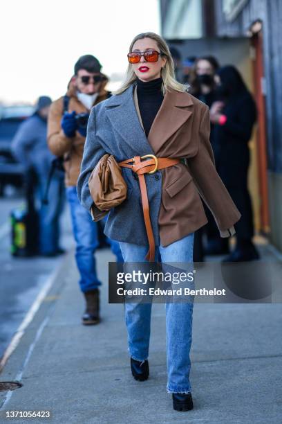 Guest wears orange sunglasses, a black turtleneck pullover, a half brown and half gray oversized blazer jacket, a camel shiny leather belt, a brown...